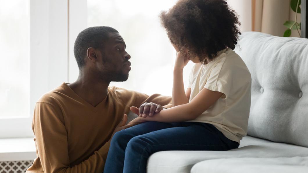 Young girl on couch being consoled by man.