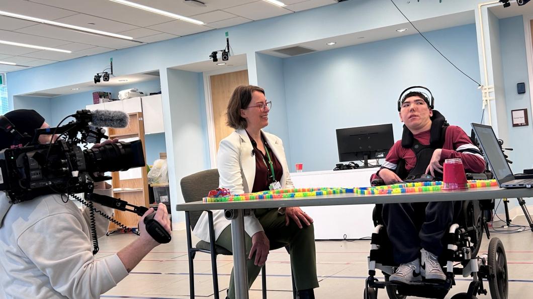 reporter with a camera is filming a clinician and a teen using brain computer interface