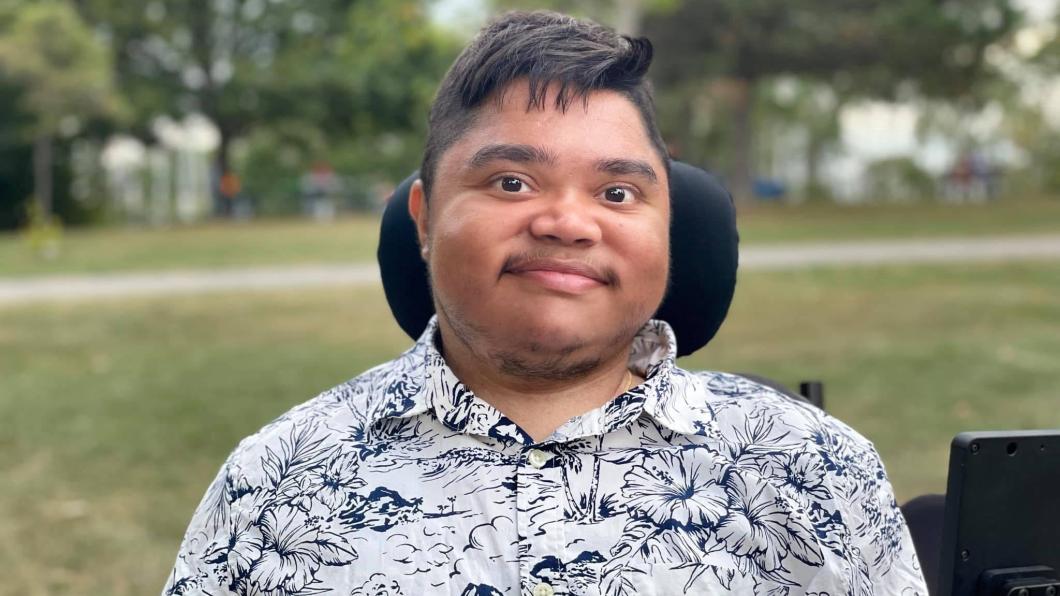 Man with dark hair in wheelchair smiles in park