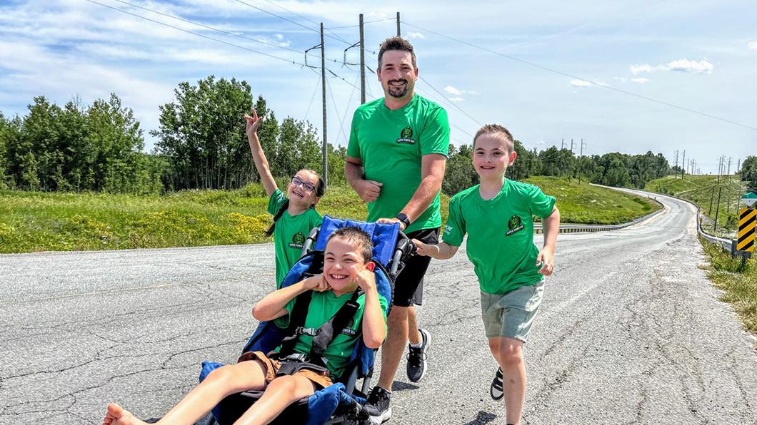 A dad and three children run together outdoors using an adapted stroller