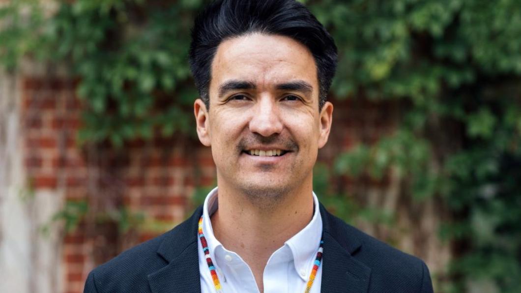 Man with dark hair and colourful necklace