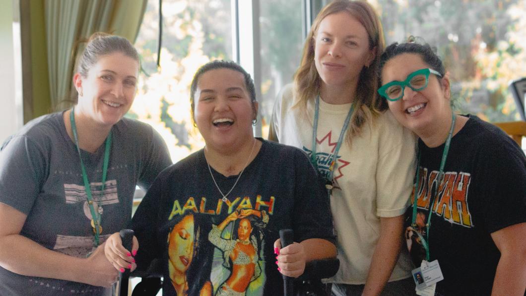 Teen wearing bright shirt and using walker surrounded by three women