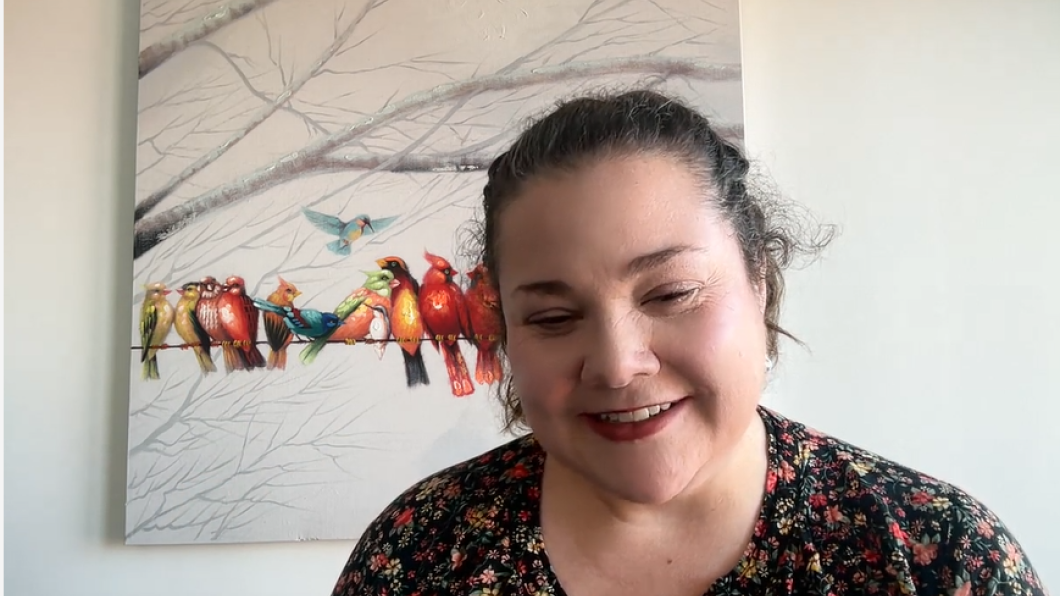 Woman with dark hair smiles on zoom screen with picture or birds behind