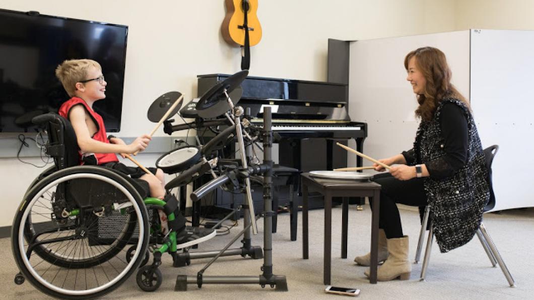 Woman teaching boy in wheelchair to play drums