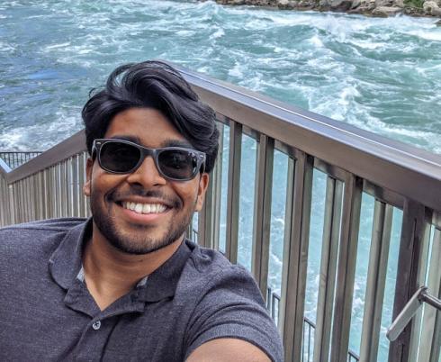Hisham smiling at the camera against a backdrop of a river behind him. 