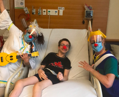Andrew in bed with a red nose, with the therapeutic clowns posing by his bedside.