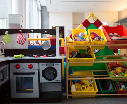Bins of red and yellow children's toys. The toys are on a shelf next to black-and-white toy kitchen appliances, including a sink, microwave and washing machine.