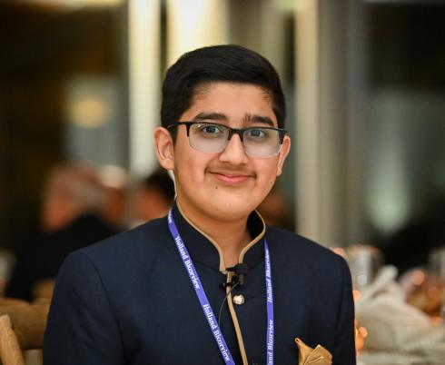 A teen with medium skin tone and short black hair wearing glasses, a blue shirt and a blue lanyard.