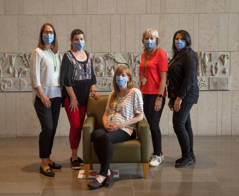 Five Holland Bloorview award winners are featured in a line against a beige wall. One staff member sits on a chair in the middle. 