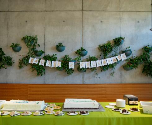 Salute and Celebrate paper banner hangs in the hospital cafeteria above two large slab cakes.
