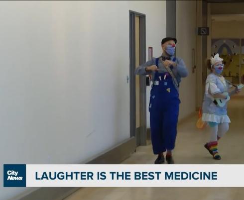 Two of our therapeutic clowns dancing and playing ukulele in a Holland Bloorview hallway