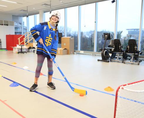 A child holding a hockey stick in front of a hockey net, wearing a helmet and ankle brace.