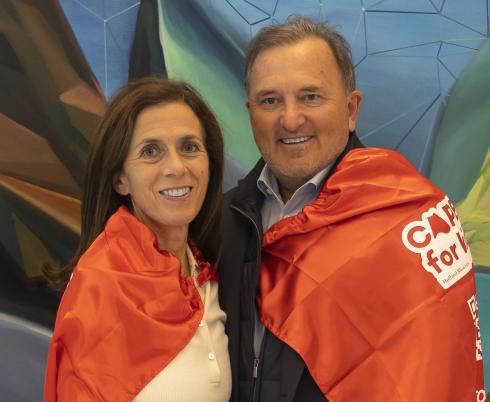 Two adults wearing red capes and standing in front of a colourful wall.