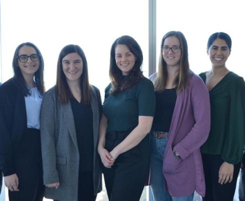 A group of researchers smile as they stand together in front of a brightly-lit window.