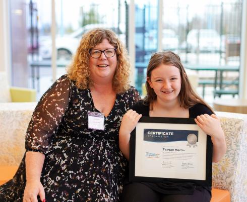 Dr. Carolyn Hunt and a child sitting beside each other on a couch. The child is holding up a framed certificate, and they are both smiling