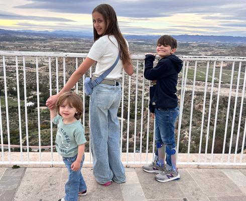 An older sister and her two younger brothers stand on a balcony.