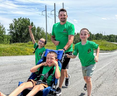 A dad and three children run together outdoors using an adapted stroller
