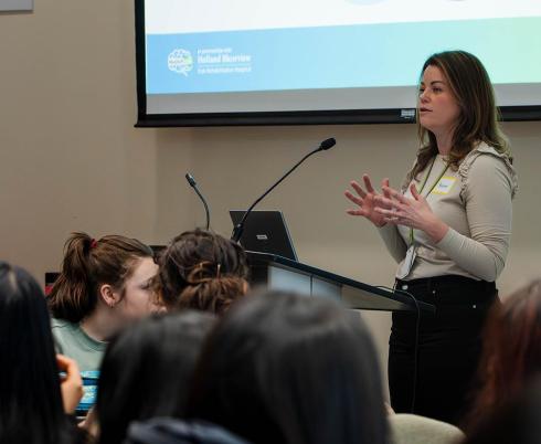 A speaker standing in front of a group of people, in a talk