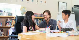 A youth and teacher are looking at each other seated at a classroom table